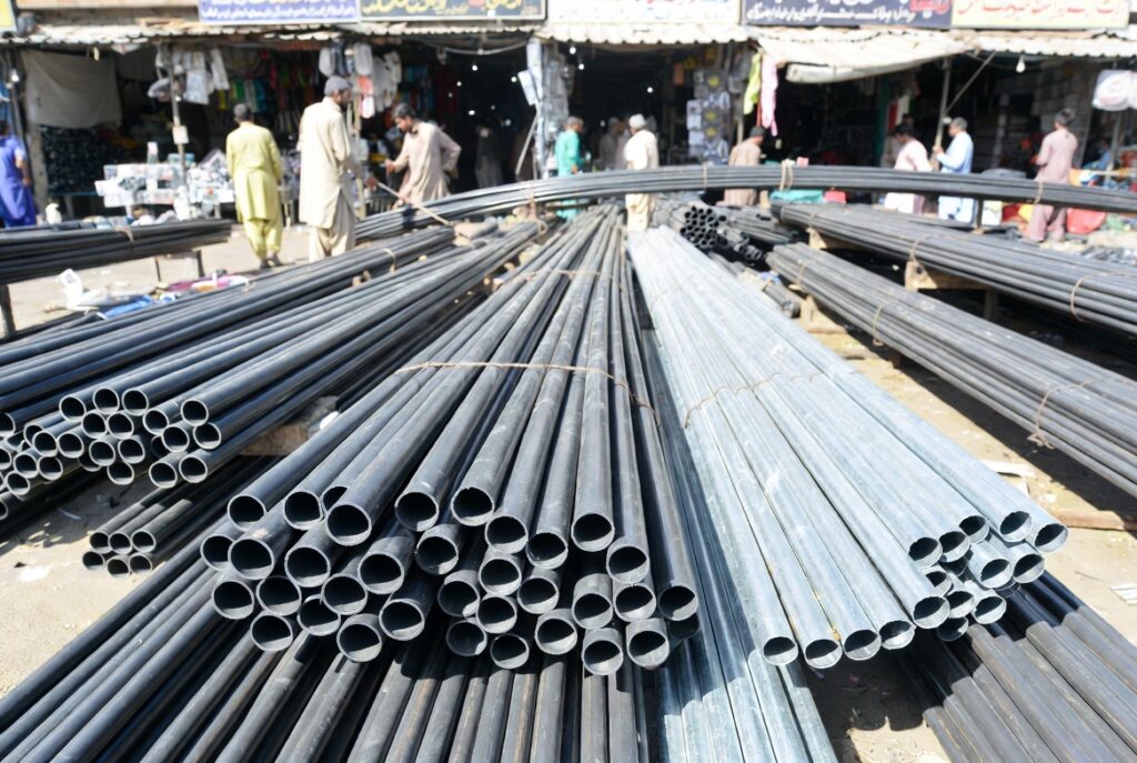 Electrical Conduit Pipes Pakistan: Types & Buying Guide 2 Electrical conduit pipes stacked in a vibrant Pakistani market with workers in traditional attire handling PVC and metal conduits under bright sunlight.
