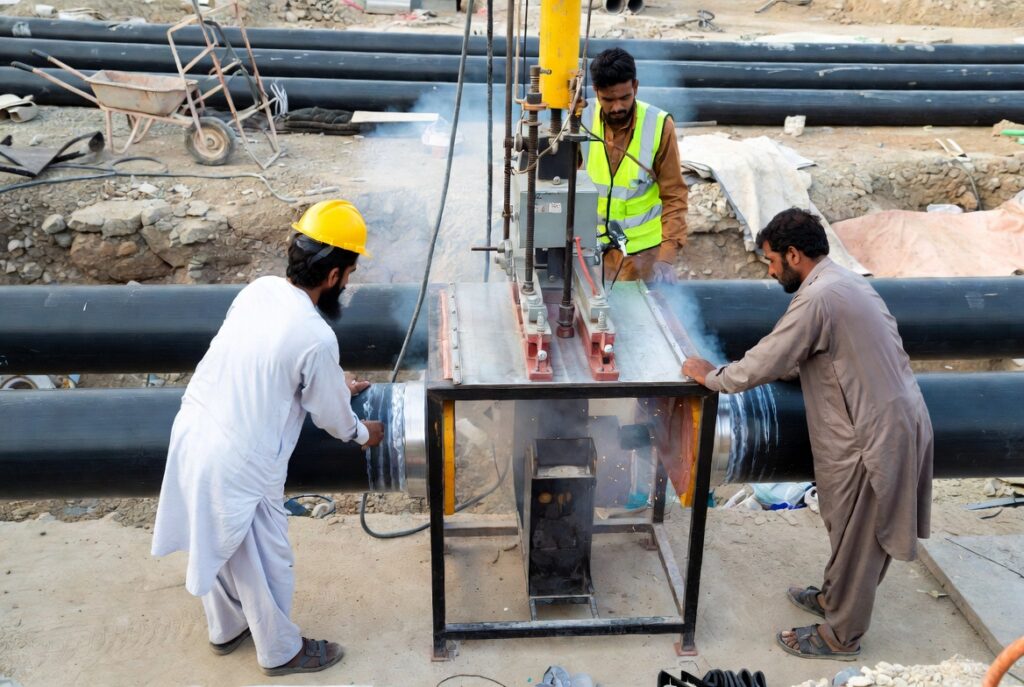 HDPE Butt-Fusion Welding: Process, Machines & Common Mistakes to Avoid 1 HDPE butt fusion welding process on a construction site in Pakistan with workers operating a machine to join large black HDPE pipes.