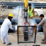 HDPE butt fusion welding process on a construction site in Pakistan with workers operating a machine to join large black HDPE pipes.