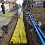 MDPE pipes laid in a trench during gas and water infrastructure installation on a Pakistani residential street with local workers handling yellow gas lines and blue water lines